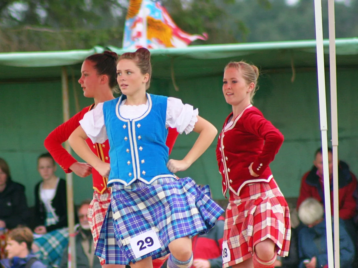 Highland dancers in kilted competition dress mid-step at a Scottish games